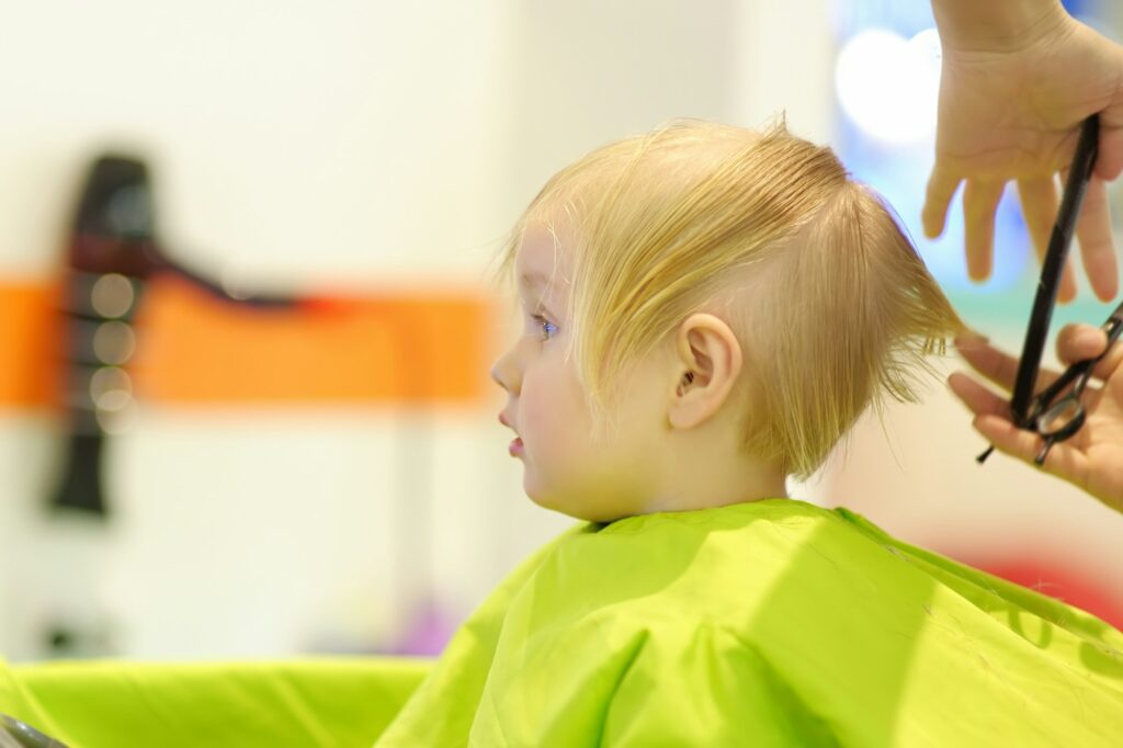 Preschooler boy getting haircut. Children hairdresser with professional tools - comb and scissors.