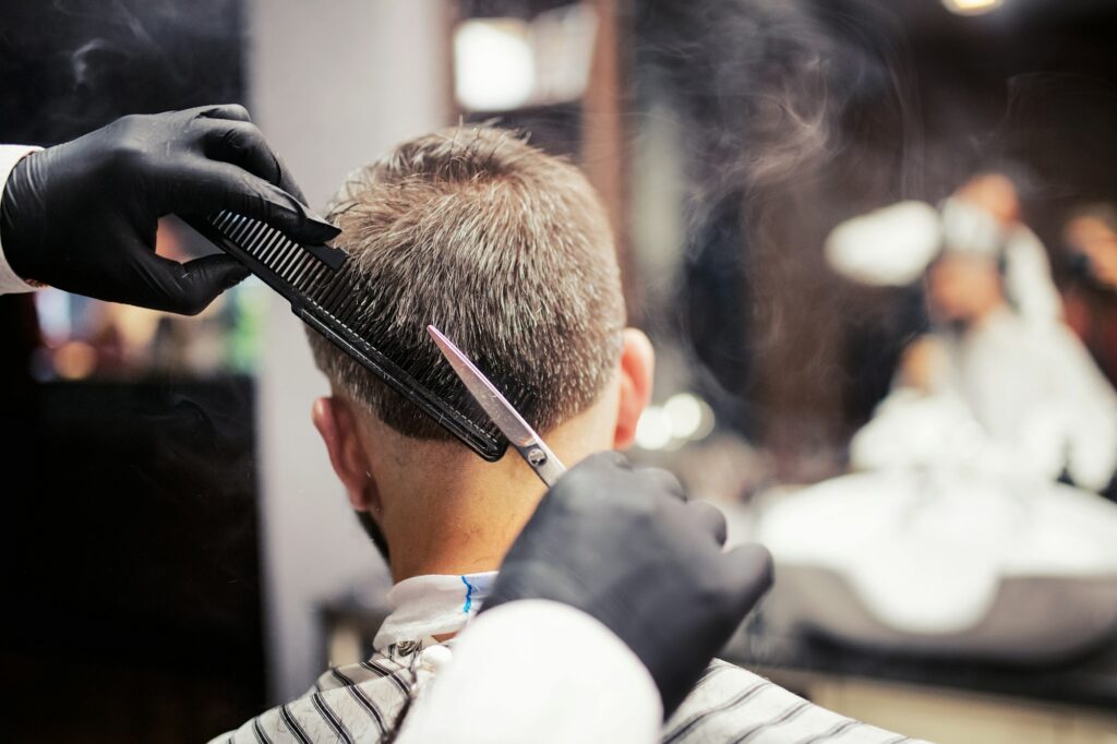 Rear view of man client visiting haidresser and hairstylist in barber shop.